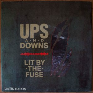 The front sleeve design of the vinyl 7" single "Lit By The Fuse" by Ups And Downs, designed by Volition