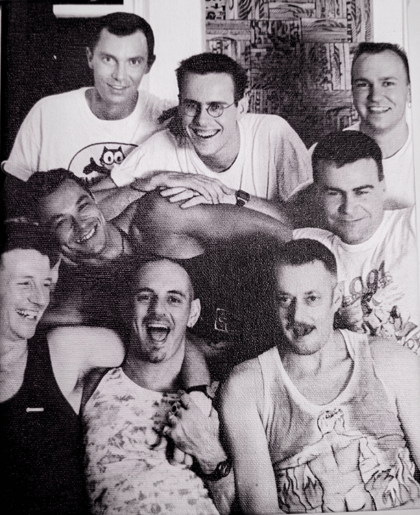 A group of nine men posing together, smiling and laughing, in a casual setting.